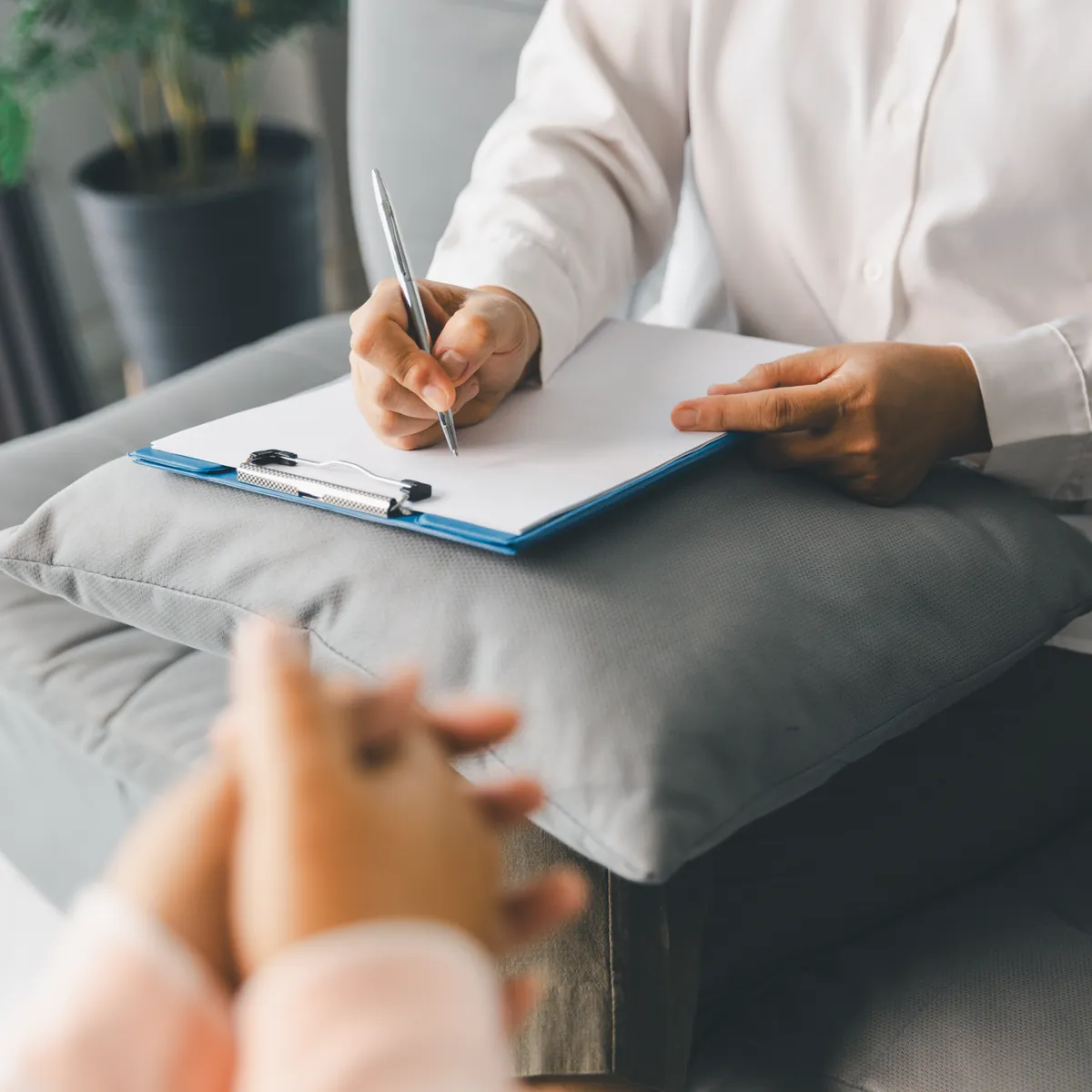 Psicóloga tomando notas en una sesión de terapia individual mientras escucha a su paciente